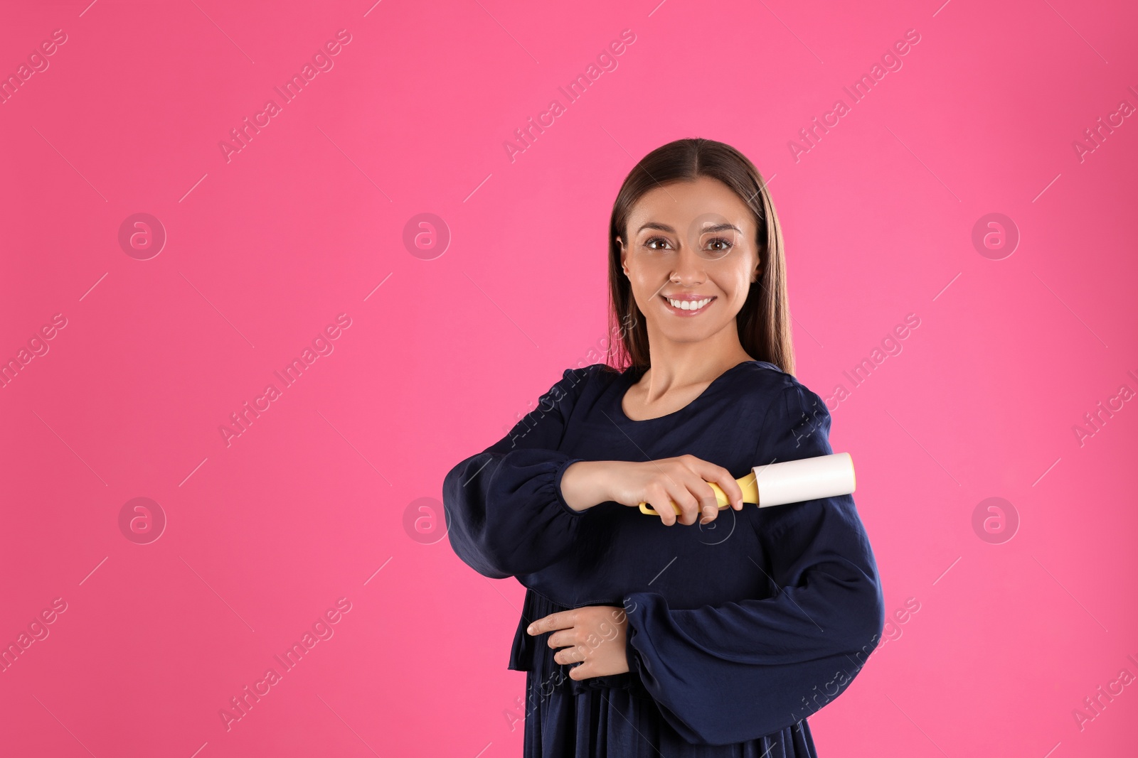 Photo of Young woman cleaning clothes with lint roller on pink background. Space for text