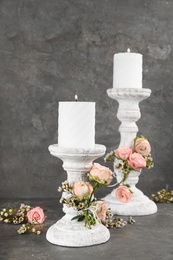 Photo of White wooden candlesticks with burning candles and floral decor on grey stone table