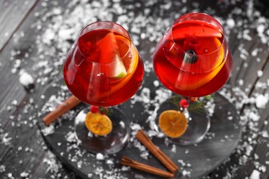 Photo of Christmas Sangria cocktail in glasses and snow on dark wooden table, closeup