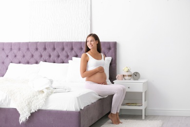 Happy pregnant woman sitting on bed at home