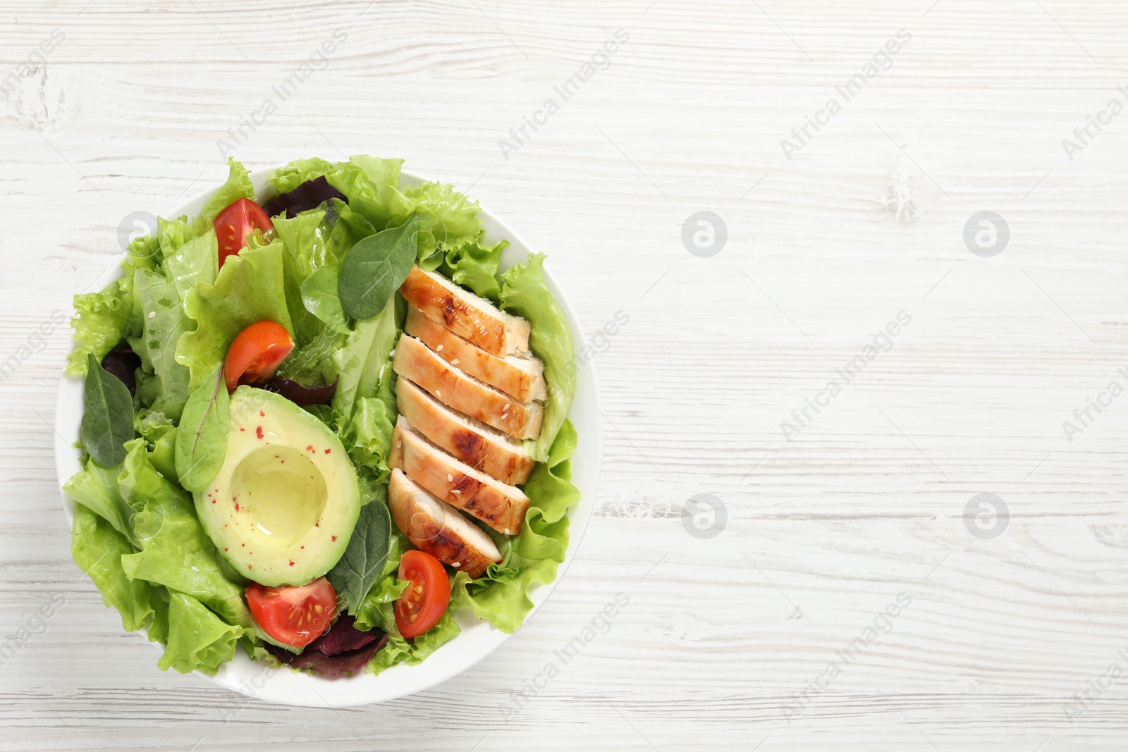 Photo of Delicious salad with chicken, cherry tomato and avocado on white wooden table, top view. Space for text