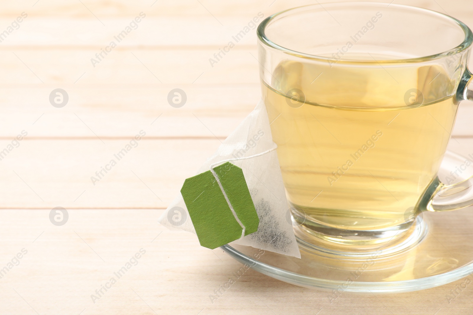 Photo of Tea bag and glass cup on light wooden table, closeup. Space for text