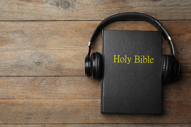 Photo of Bible and headphones on wooden background, top view with space for text. Religious audiobook