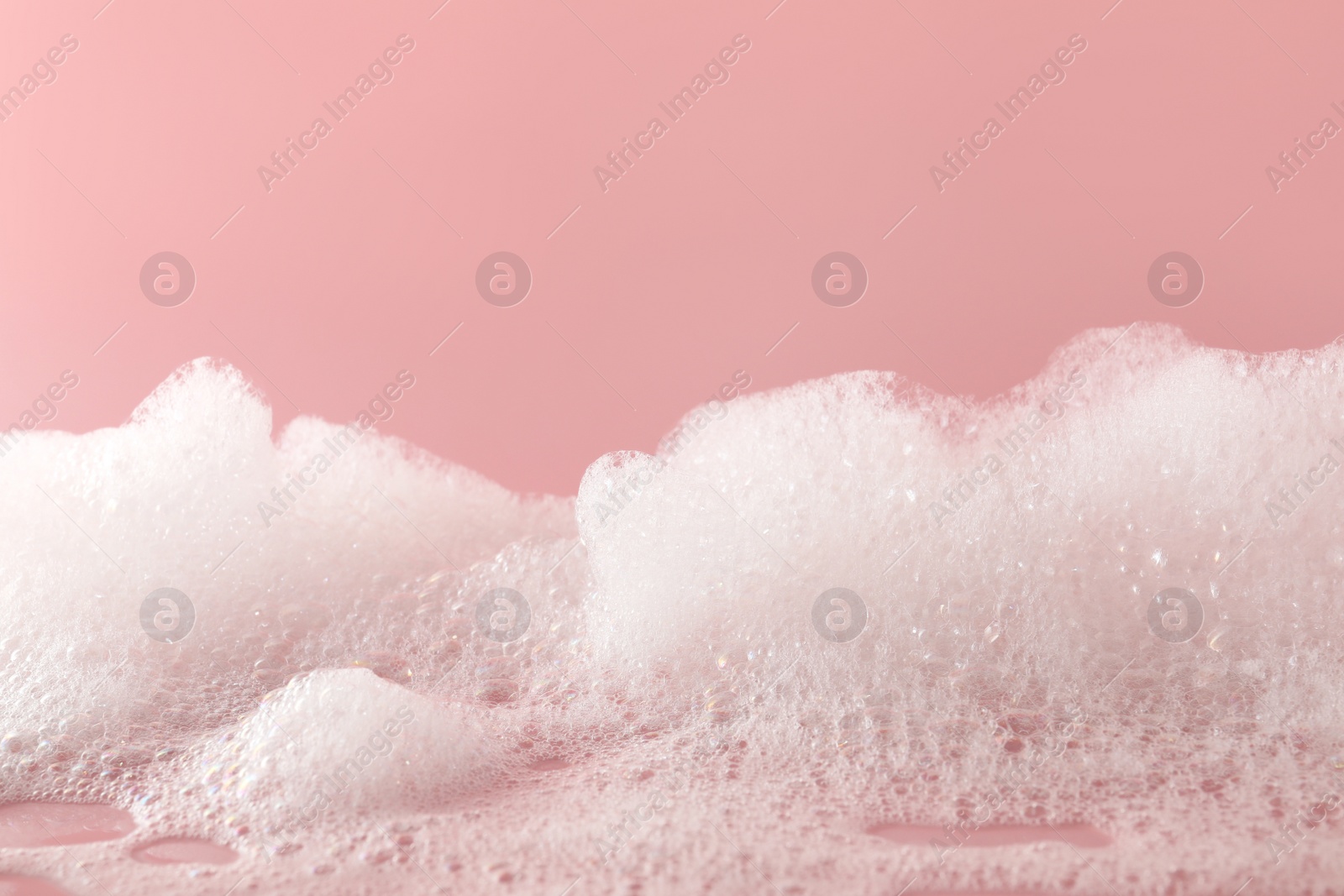 Photo of Fluffy bath foam on pink background, closeup