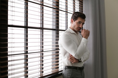 Photo of Handsome young man in white shirt standing near window indoors