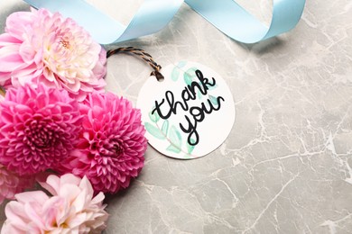 Photo of Paper tag with phrase Thank You and bouquet of dahlias on marble table, flat lay