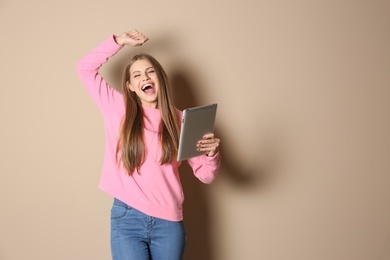 Photo of Emotional young woman with tablet celebrating victory on color background. Space for text