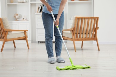 Woman cleaning dirty white parquet floor with mop at home, closeup