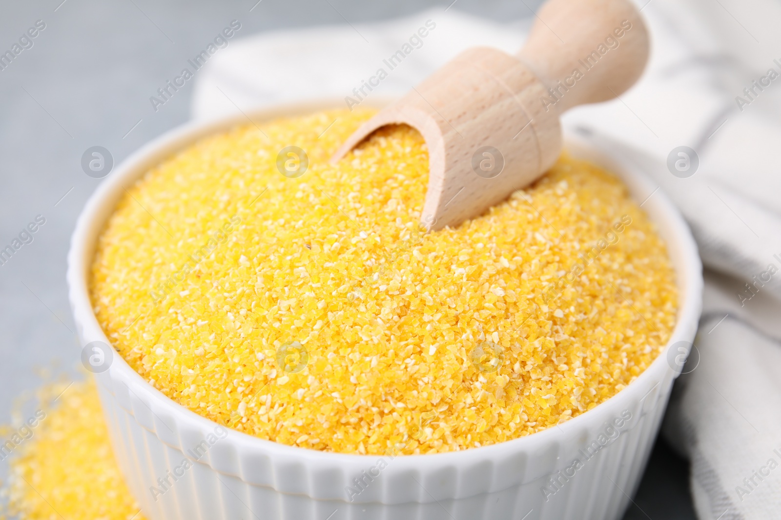 Photo of Raw cornmeal and scoop in bowl on grey table, closeup