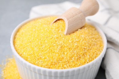 Raw cornmeal and scoop in bowl on grey table, closeup
