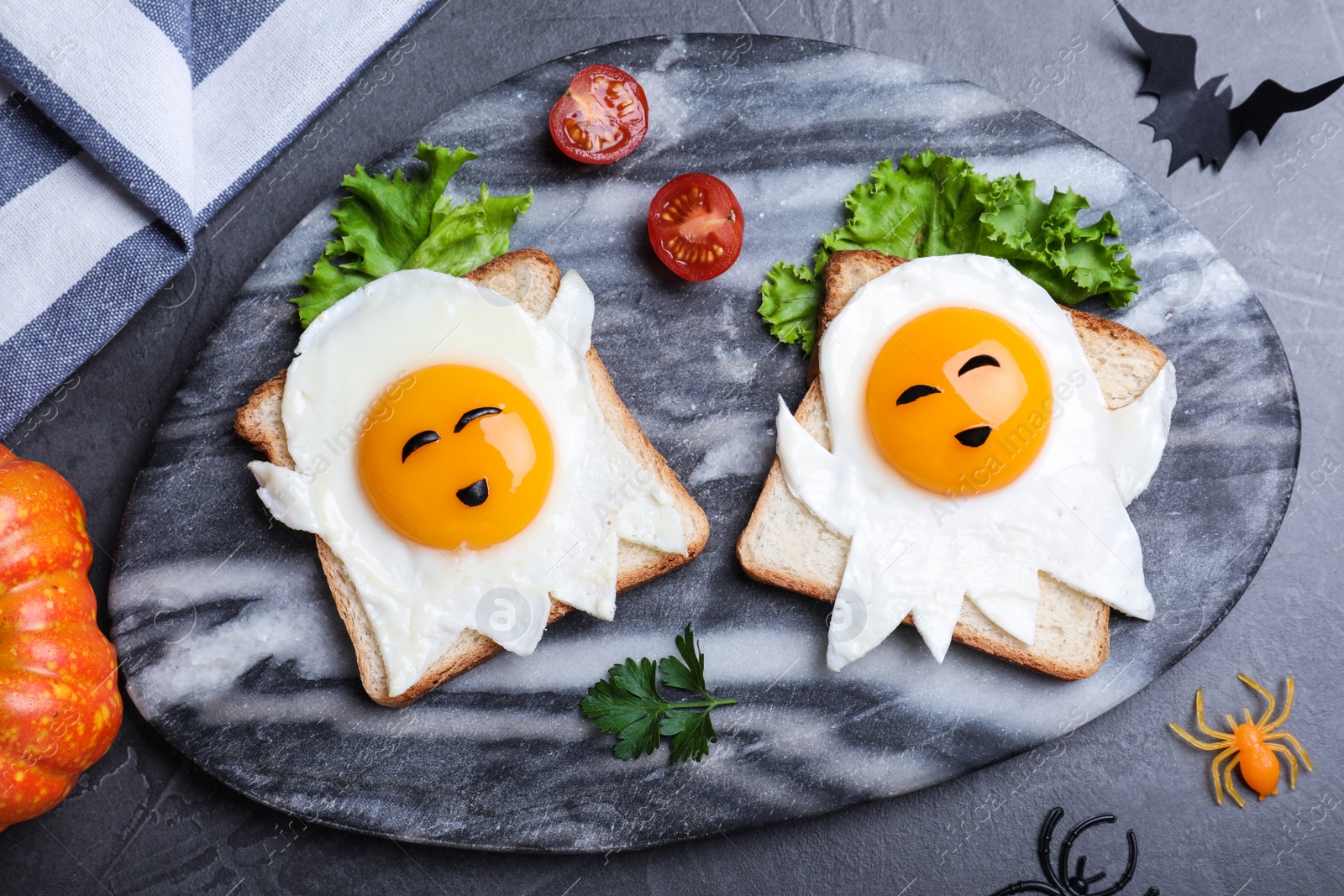 Photo of Halloween themed breakfast served on black table, flat lay. Tasty toasts with fried eggs in shape of ghost