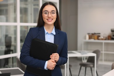 Photo of Happy real estate agent with leather portfolio indoors. Space for text