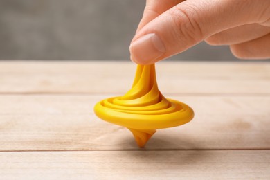Photo of Woman playing with yellow spinning top at light wooden table, closeup