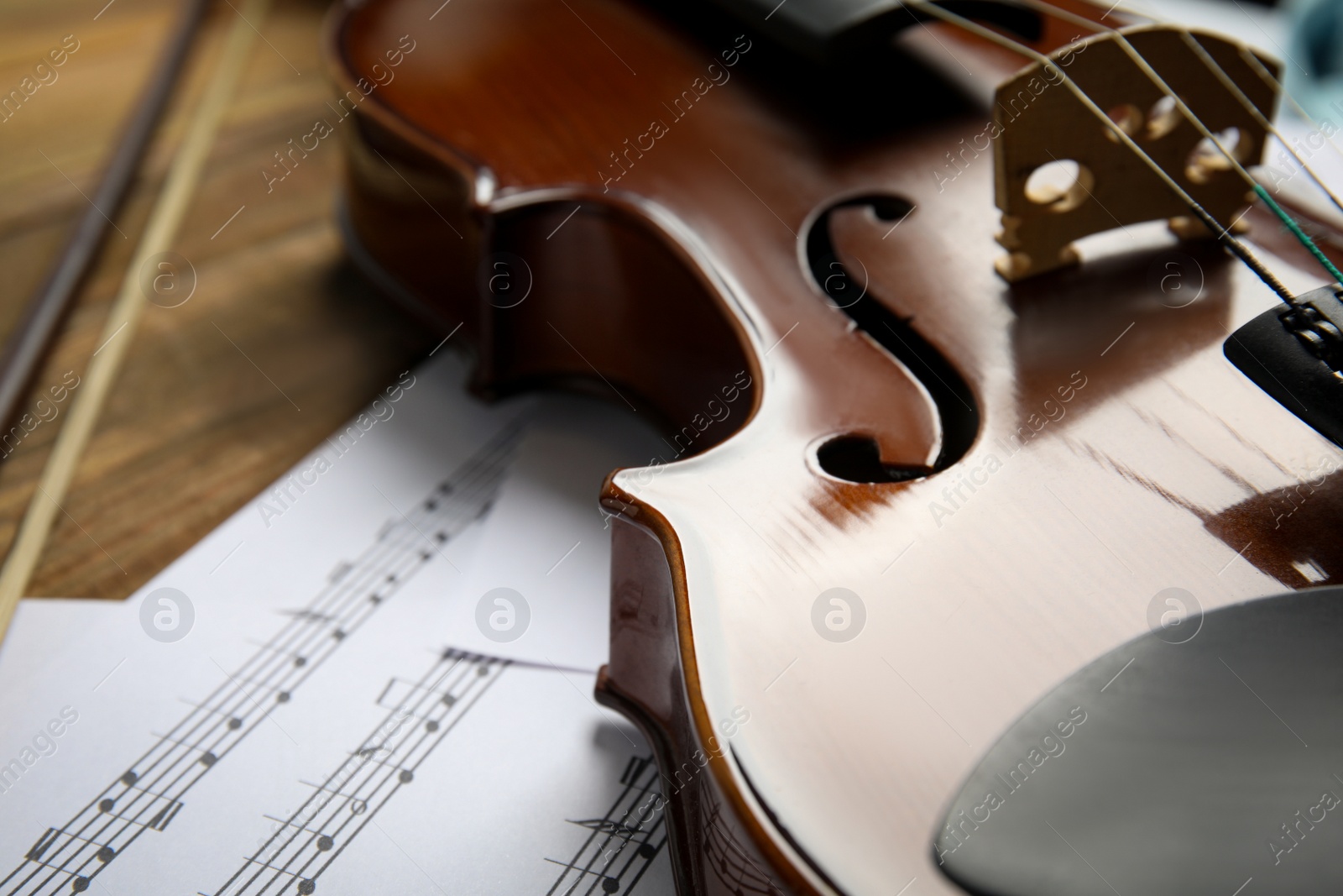Photo of Beautiful violin, bow and note sheets on wooden table, closeup