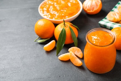 Tasty tangerine jam in glass jar on dark table, space for text