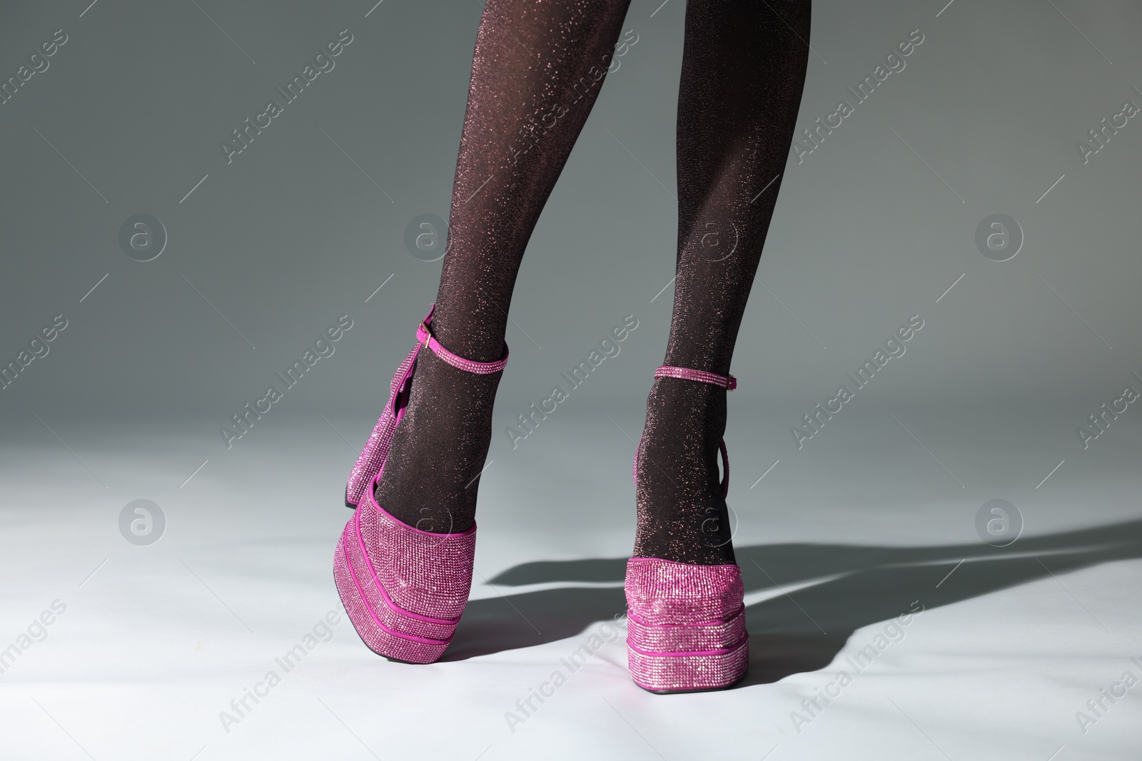 Photo of Woman wearing pink high heeled shoes with platform and square toes on light grey background, closeup