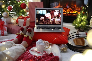 Photo of MYKOLAIV, UKRAINE - DECEMBER 23, 2020: Woman watching The Queen's Gambit series on laptop near fireplace at home, closeup. Cozy winter holidays atmosphere
