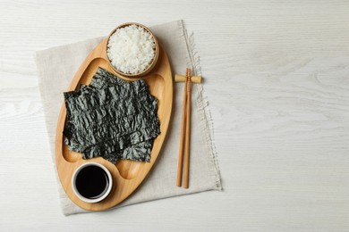 Dry nori sheets, rice, soy sauce and chopsticks on white wooden table, top view. Space for text