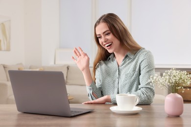 Photo of Happy woman having video chat via laptop at wooden table