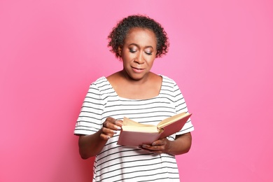 Portrait if mature African-American woman reading book on pink background