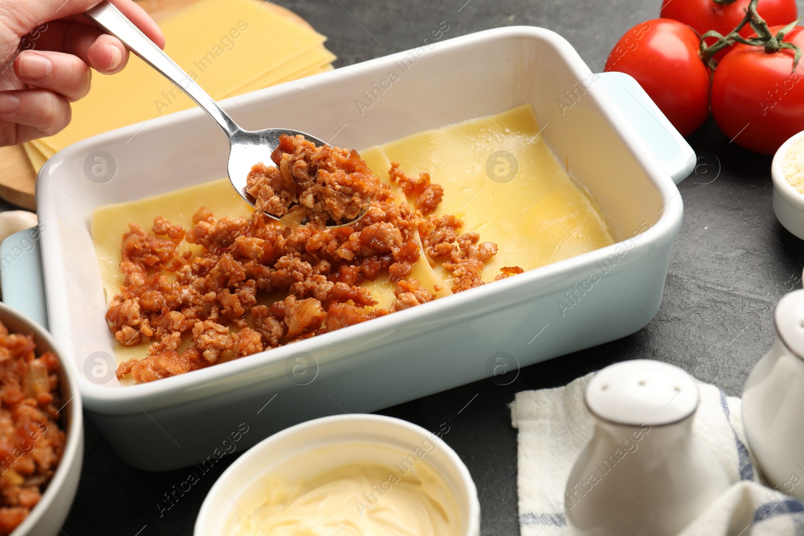 Photo of Woman making lasagna at dark table, closeup