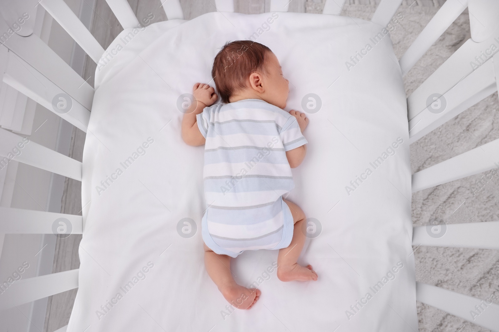 Photo of Cute newborn baby sleeping in crib at home, top view. Bedtime