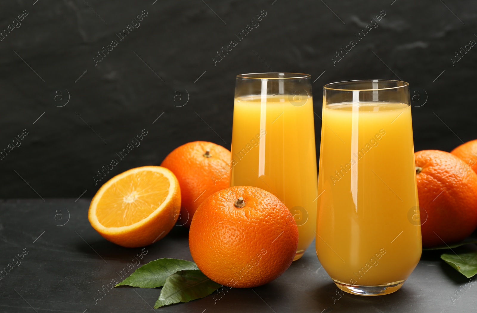 Photo of Delicious orange juice and fresh fruits on black table