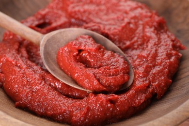 Photo of Spoon with tasty tomato paste in wooden bowl, closeup