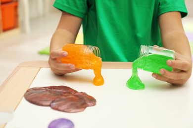 Photo of Little boy pouring slime onto table indoors, closeup