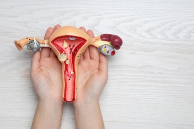 Photo of Woman with anatomical model of uterus at white wooden table, top view and space for text. Gynecology concept