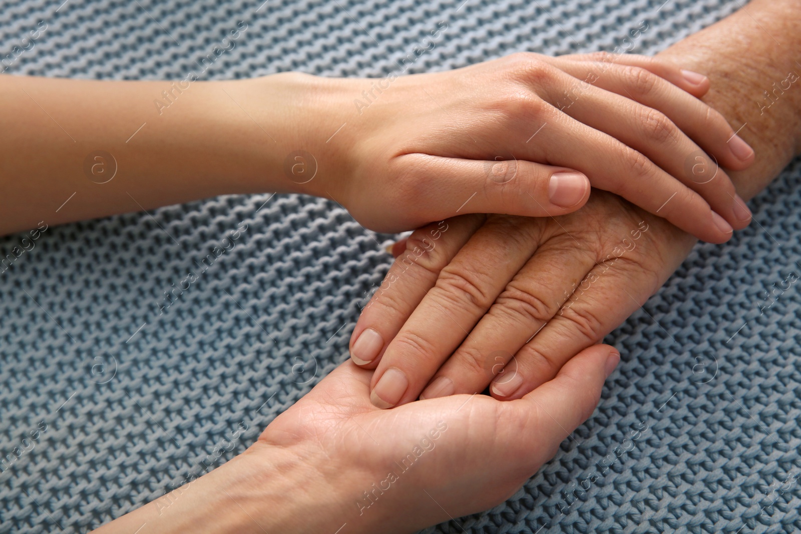 Photo of Young and elderly women holding hands together on grey fabric, closeup