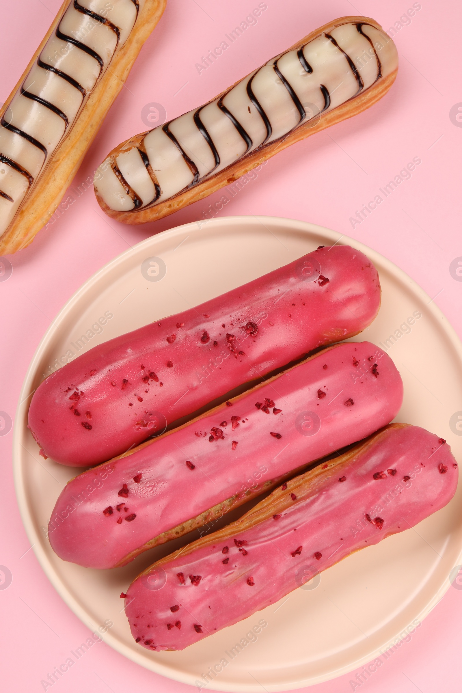 Photo of Delicious eclairs covered with glaze on pink background, flat lay