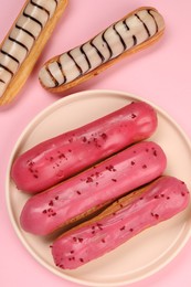 Delicious eclairs covered with glaze on pink background, flat lay