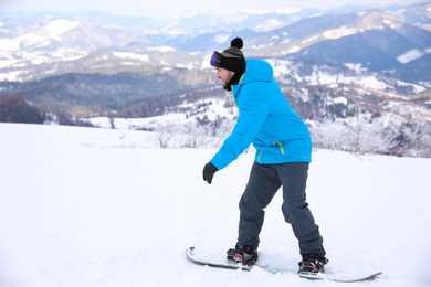 Young man with snowboard on hill at mountain resort. Winter vacation