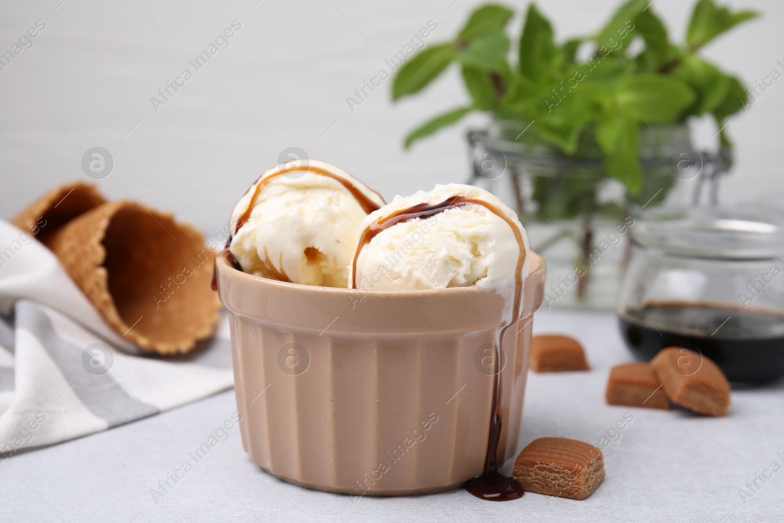 Photo of Scoops of ice cream with caramel sauce and candies on light grey table, closeup