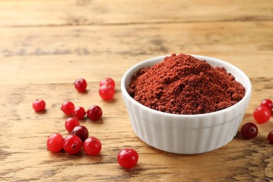 Photo of Dried cranberry powder in bowl and fresh berries on wooden table, closeup. Space for text