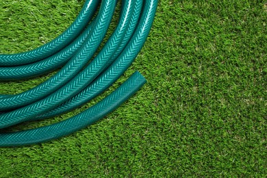 Photo of Watering hose on green grass, top view. Space for text