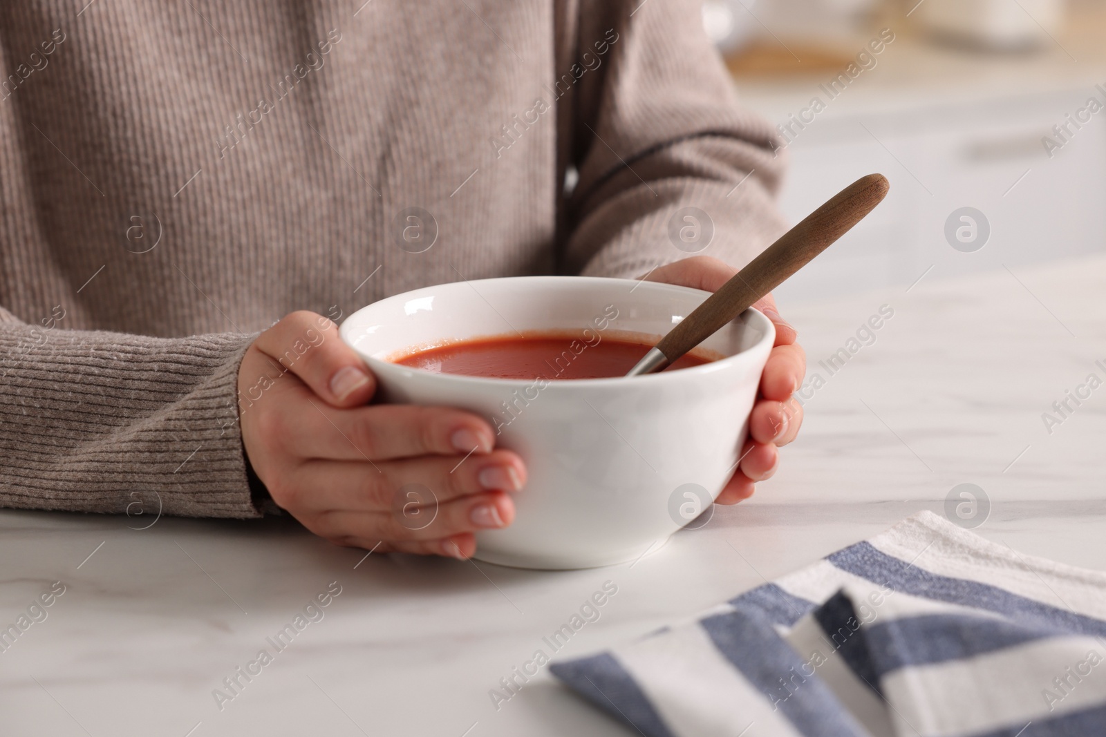 Photo of Woman eating tasty tomato soup at white marble table, closeup