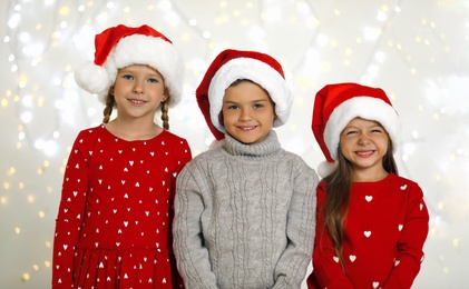 Photo of Happy little children in Santa hats against blurred festive lights. Christmas celebration