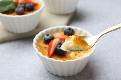 Taking delicious creme brulee with berries from bowl at grey table, closeup