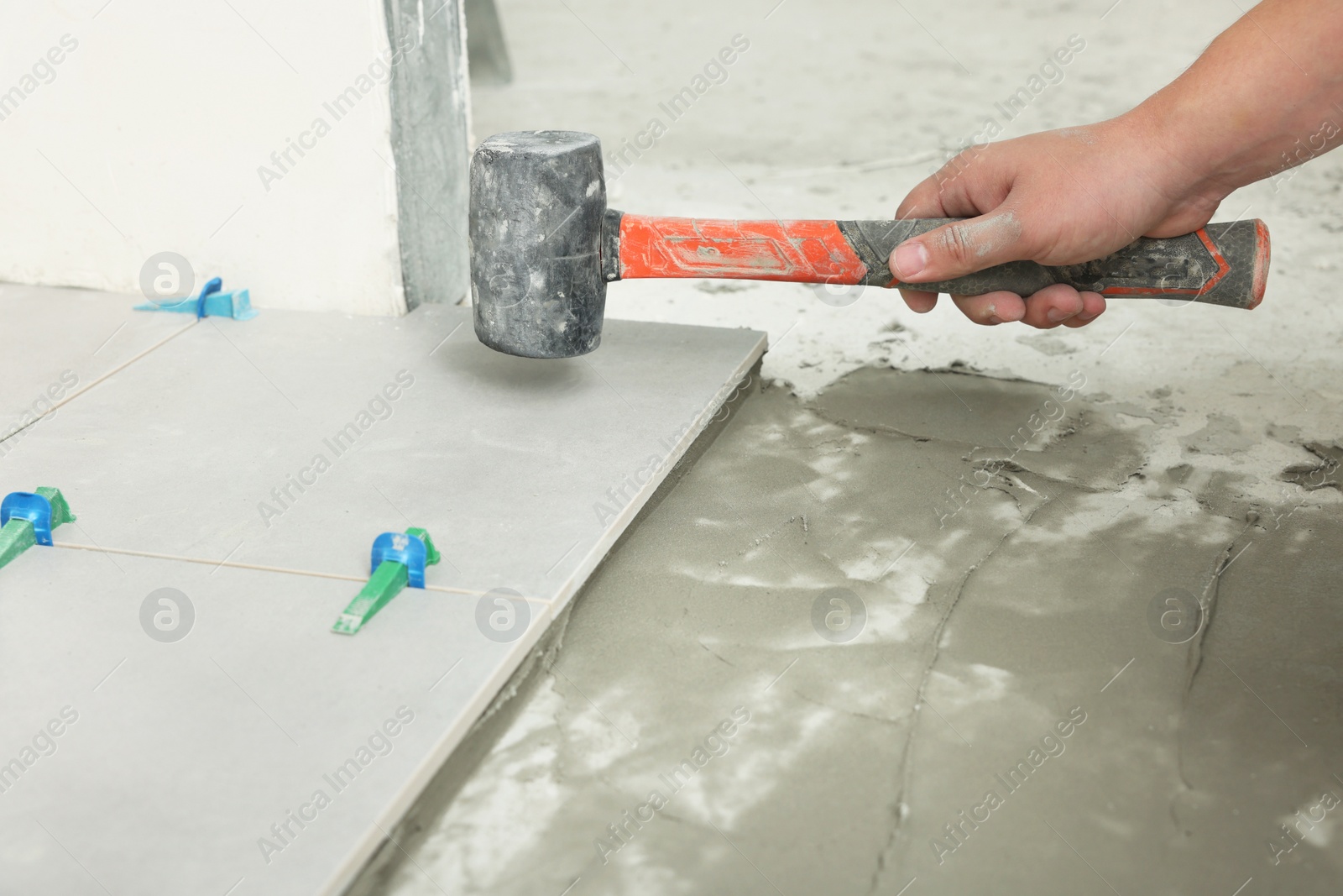 Photo of Worker with rubber hummer installing tiles indoors , closeup