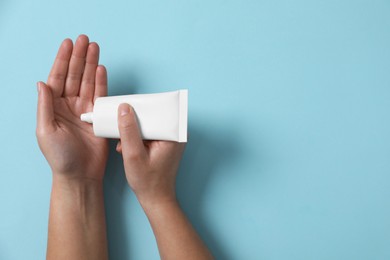 Photo of Woman applying cosmetic cream from tube onto her hand on light blue background, top view. Space for text