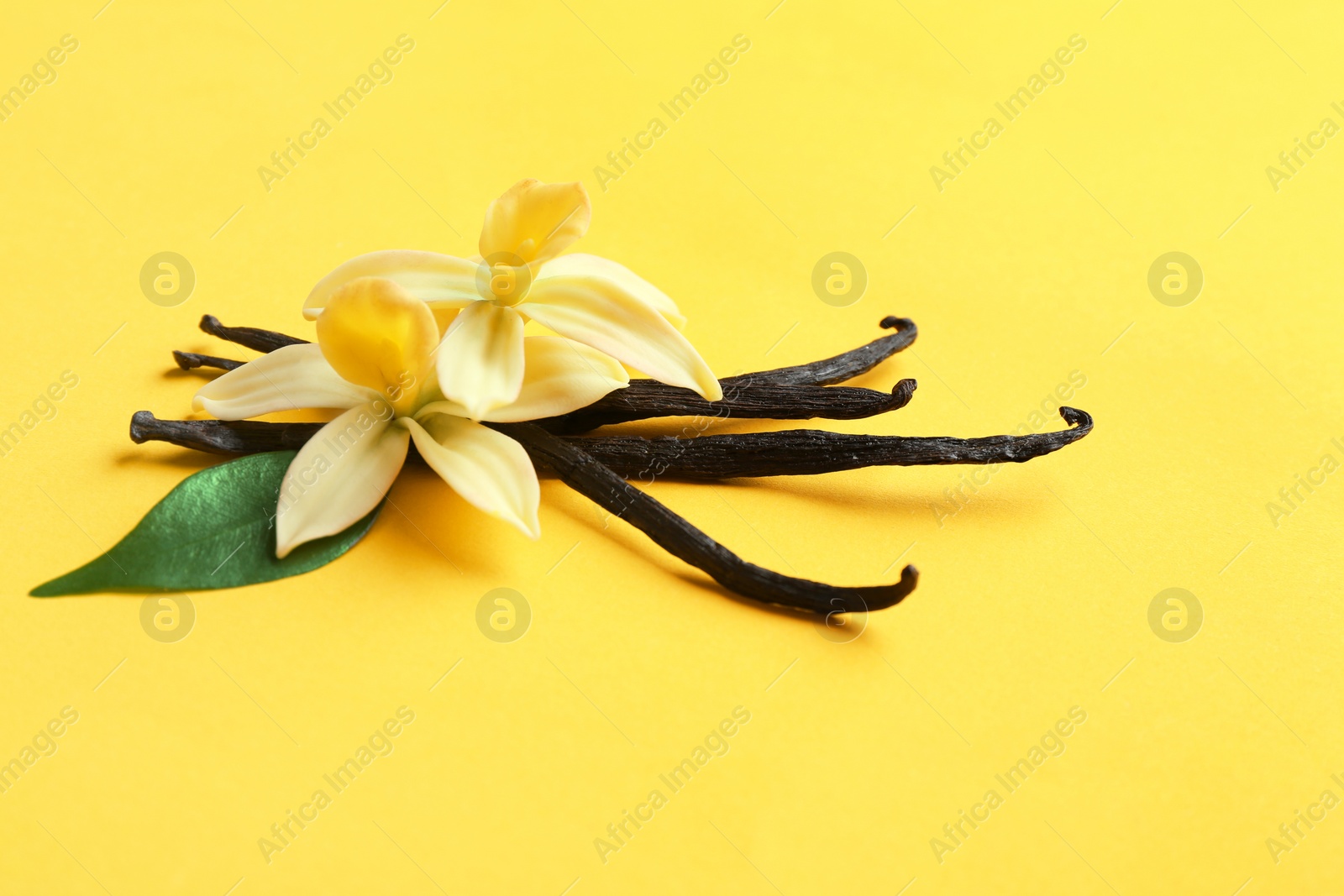 Photo of Vanilla sticks and flowers on yellow background. Space for text