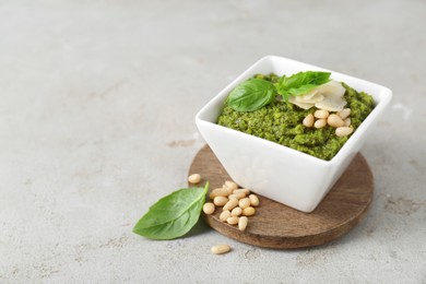 Photo of Bowl with delicious pesto sauce, cheese, pine nuts and basil leaves on light table, closeup. Space for text