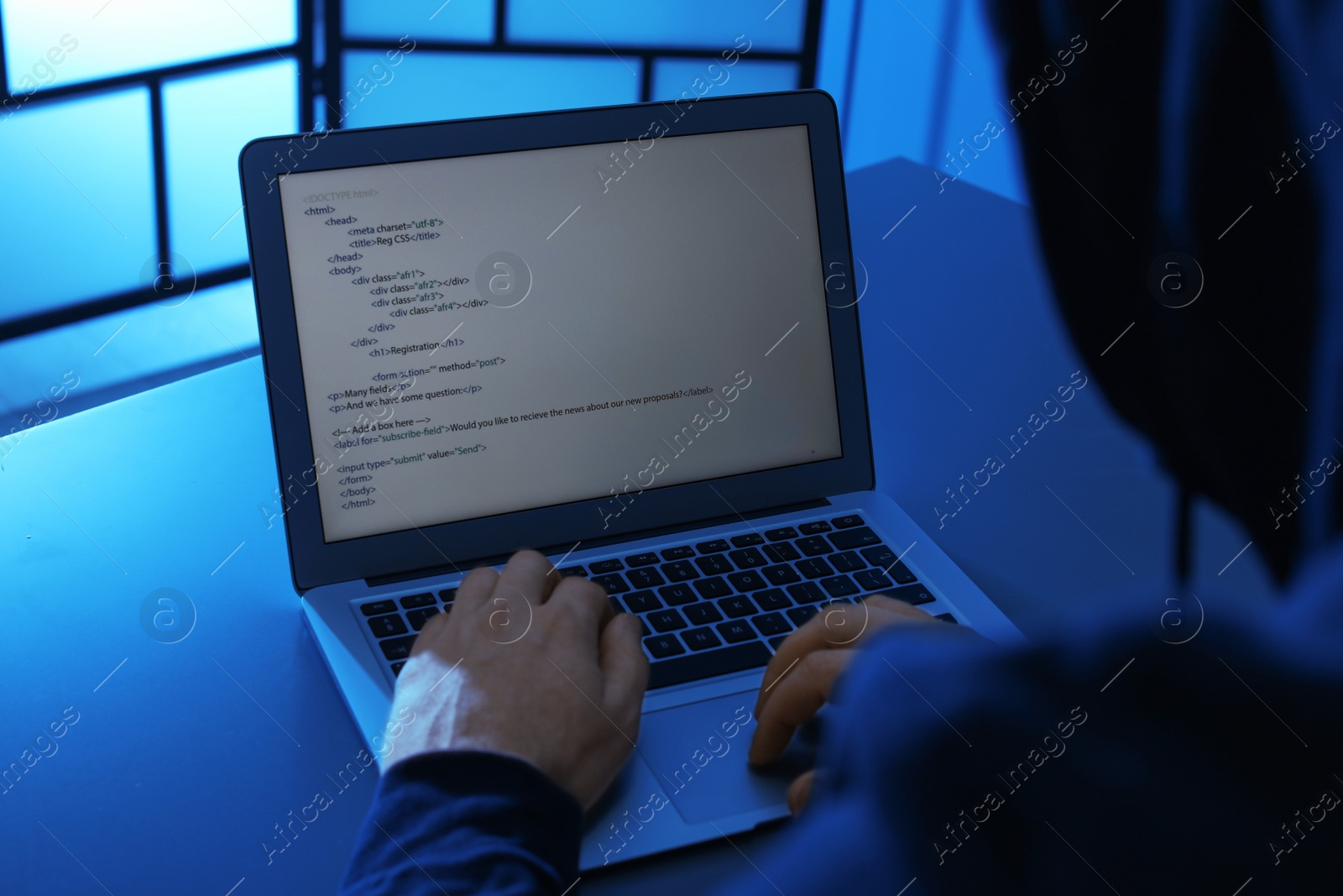 Photo of Man using laptop at table in dark room, closeup. Criminal offence