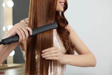 Young woman using hair iron indoors, closeup