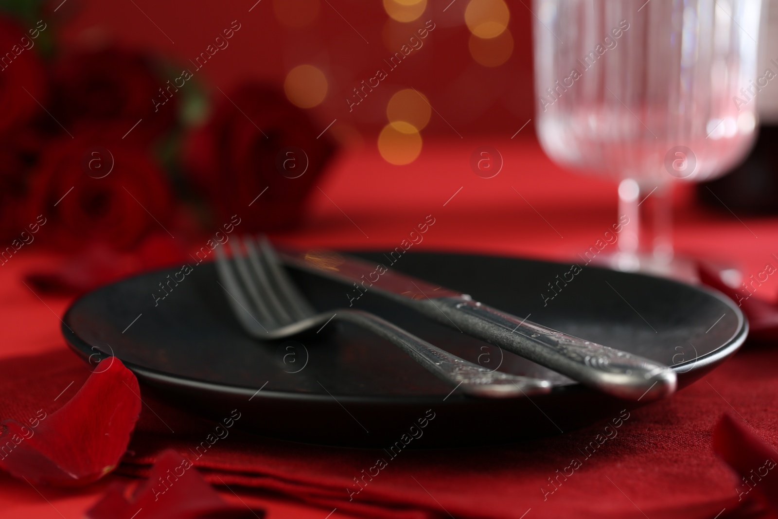 Photo of Place setting with roses on red table, closeup. Romantic dinner