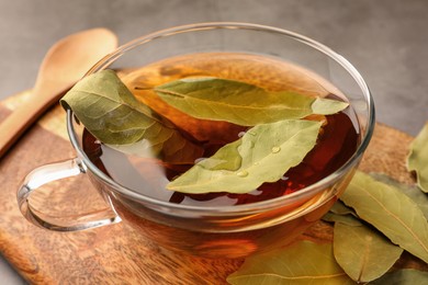 Photo of Cup of freshly brewed tea with bay leaves on wooden board, closeup