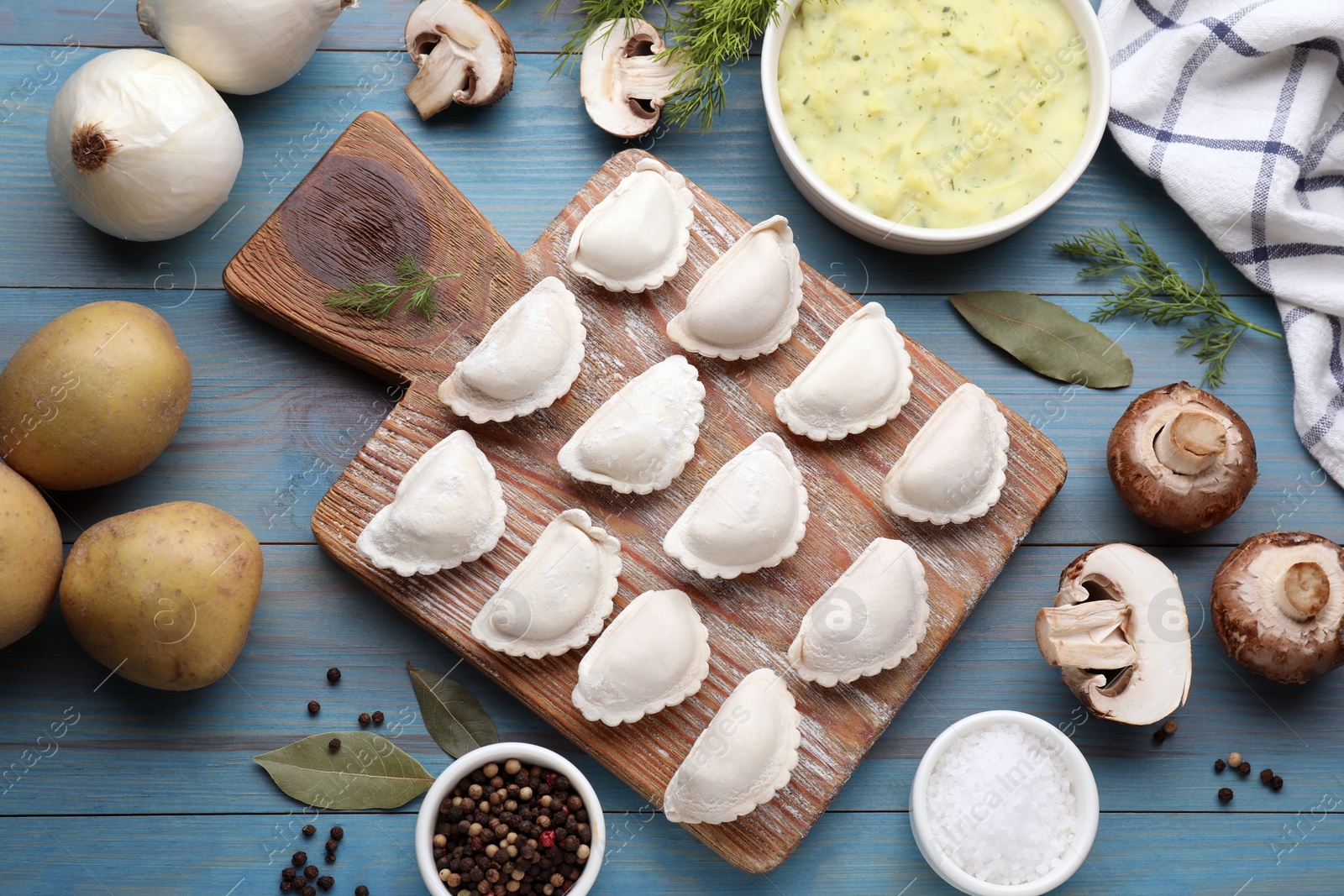 Photo of Raw dumplings (varenyky) and ingredients on light blue table, flat lay