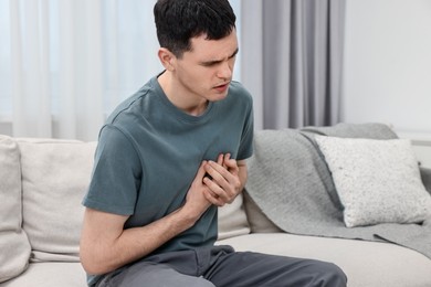 Young man suffering from heart hurt on sofa at home